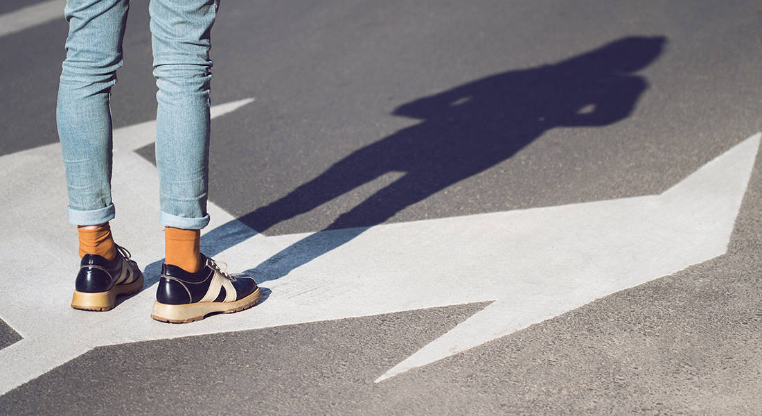 side view close up of a young woman wearing black shoes and blue jeans standing on a street with arrow signs pointing in different directions concept for life choices